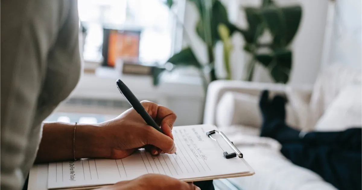 A caregiver writing on a clipboard at a patient's bedside in a skilled nursing facility